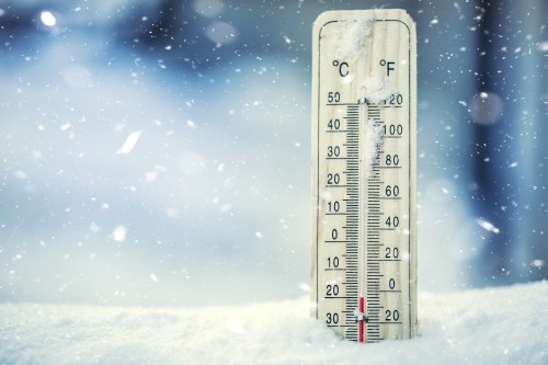 A thermometer in the snow shows a temperature below freezing, with snowflakes falling around it.