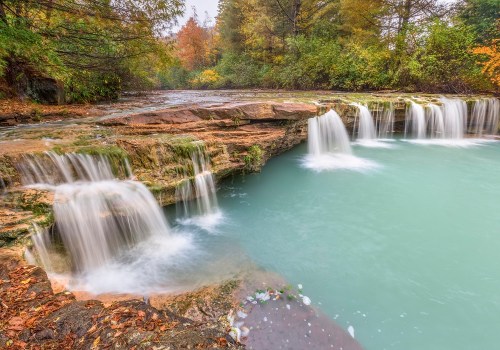 A serene waterfall cascades over rocky ledges into a turquoise pool, surrounded by autumn foliage and lush greenery.