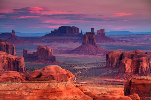 A stunning desert landscape at sunset, featuring red rock formations and distant mesas under a colorful sky.