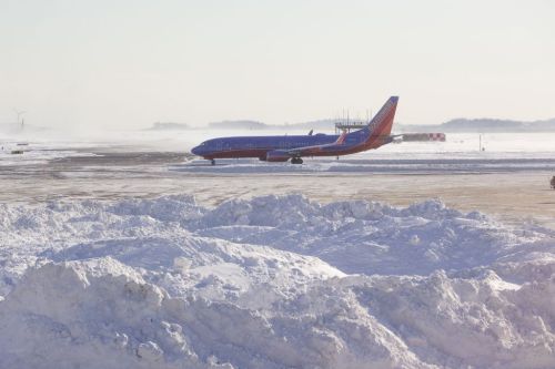 A Southwest Airlines plane taxiing on a snowy runway, with large snowdrifts in the foreground.