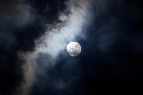 A bright full moon partially obscured by dark, swirling clouds in a night sky.