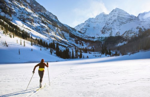 A person cross-country skiing on a snowy landscape with mountains in the background.
