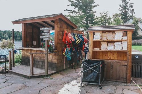 A rustic kiosk by a lake offers snacks and ice cream, with life jackets hanging nearby and towels stacked in a wooden shed.