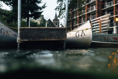 Two canoes docked at a wooden platform on a calm waterway, with a building and church tower in the background.