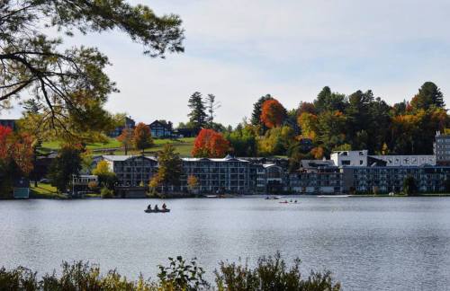 A serene lake view with colorful autumn trees and buildings along the shore, featuring people kayaking on the water.