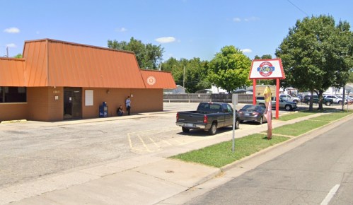 A small building with an orange roof, parking lot, and a sign for a restaurant, set against a clear blue sky.