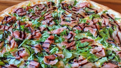 A pizza topped with arugula, prosciutto, and a drizzle of balsamic glaze.