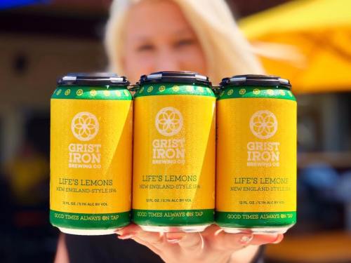 Three cans of "Life's Lemons" New England-style IPA from Grist Iron Brewing Co., held by a person outdoors.