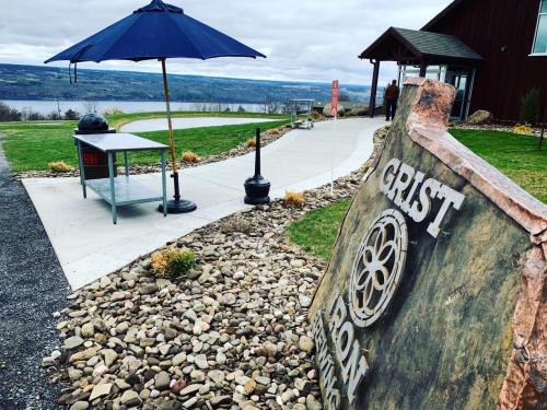 A scenic outdoor area with a sign for "Grist Iron," a table under an umbrella, and a view of the water in the background.