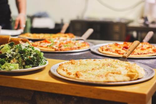 A variety of pizzas on metal trays with a side salad on a wooden table.