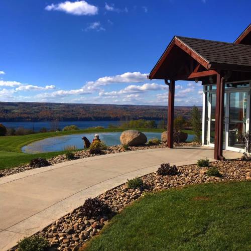 Scenic view of a landscaped yard with a pathway, rocks, and a lake under a blue sky with fluffy clouds.