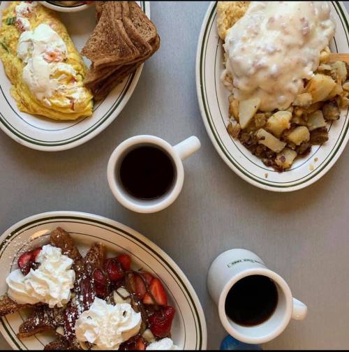 A table with two plates of breakfast: an omelette, toast, potatoes, and a plate of French toast with strawberries and whipped cream, plus coffee.