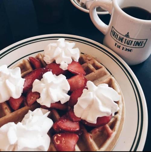 A plate of waffles topped with strawberries and whipped cream, alongside a cup of coffee.