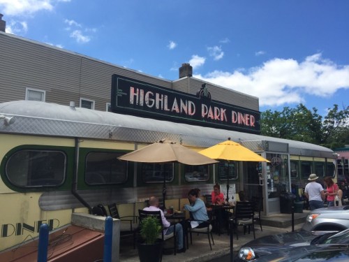 Exterior of Highland Park Diner with outdoor seating, umbrellas, and a clear blue sky in the background.