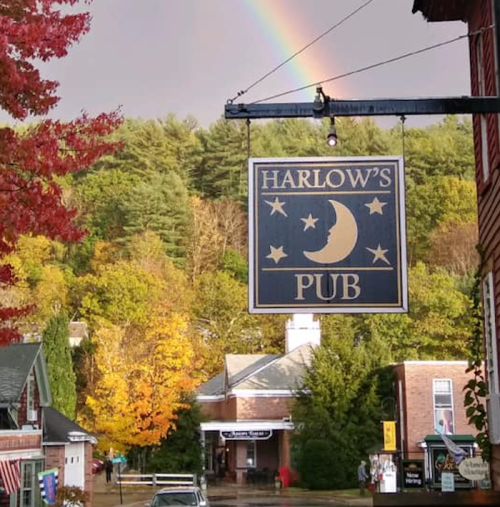A sign for Harlow's Pub hangs outside, with a rainbow and colorful autumn trees in the background.