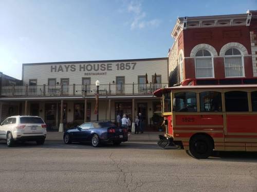 Historic Hays House 1857 restaurant with a trolley and parked cars in front, under a clear blue sky.