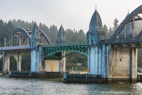A historic bridge with ornate towers spans a river, surrounded by misty trees and calm waters.