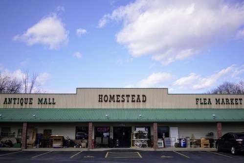 Exterior of the Homestead Antique Mall and Flea Market, featuring a green roof and cloudy blue sky.