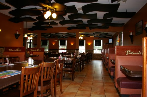 Interior of a cozy restaurant with wooden tables, chairs, and a unique ceiling design, featuring booths along the walls.