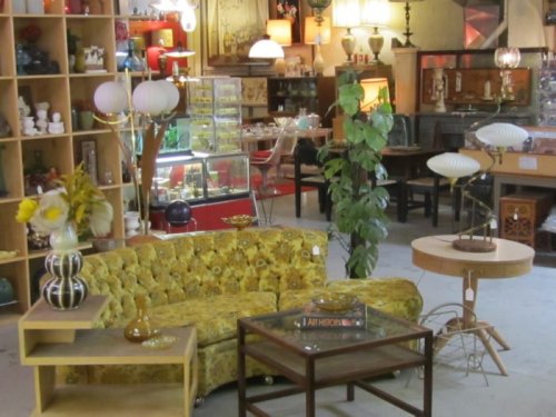 A vintage furniture store featuring a yellow couch, decorative lamps, and various retro decor items.