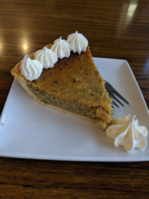 A slice of pie topped with whipped cream, served on a white plate with a fork beside it.
