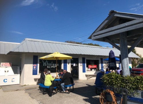 A casual outdoor dining area at Whaley's, featuring tables under umbrellas and patrons enjoying their meals.