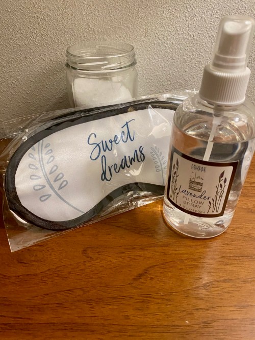 A sleep mask labeled "Sweet dreams" next to a lavender pillow spray on a wooden surface.
