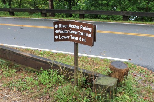 A brown wooden sign with directional arrows for River Access Parking, Visitor Center Trail (1.5 mi), and Lower Town (0.6 mi).