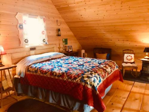 Cozy attic bedroom with wooden walls, a quilted bedspread, and warm lighting from lamps.