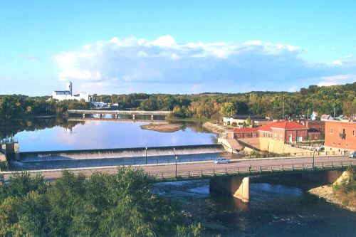 A scenic view of a river with a bridge, surrounded by trees and buildings under a clear blue sky.