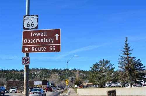 Sign for Historic Route 66 directing to Lowell Observatory, with a clear blue sky and trees in the background.