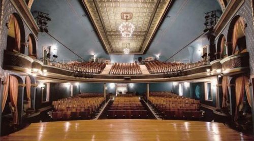 Interior of a vintage theater, featuring a spacious stage, ornate ceiling, and rows of empty seats.