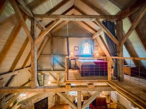 Cozy loft bedroom with wooden beams, a bed, and soft lighting, overlooking a rustic living area below.