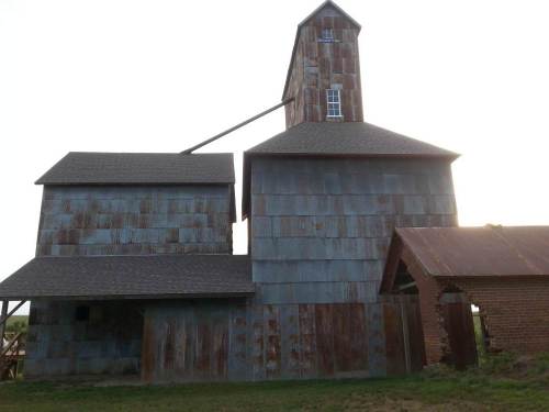 Rustic barn with a tall, weathered structure and a sloped roof, set against a soft evening sky.