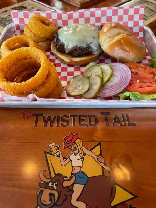 A tray with a cheeseburger, onion rings, a soft bun, lettuce, tomato, pickles, and a logo of The Twisted Tail.