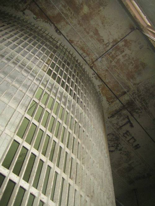 A close-up view of a rusty, curved metal structure with a grid pattern and peeling paint.