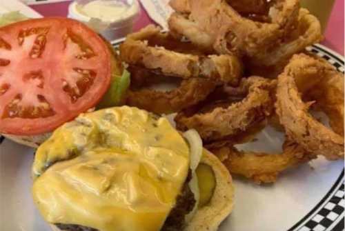 A cheeseburger with lettuce and tomato, served with a side of crispy onion rings.
