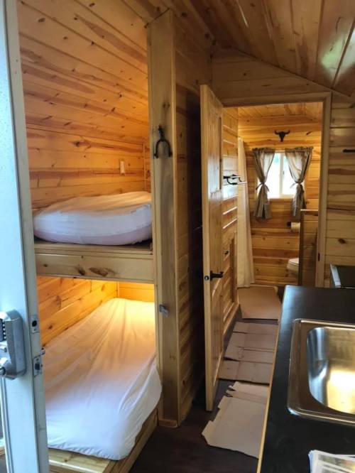Cozy wooden interior of a cabin featuring a bunk bed, a door, and a window with curtains.