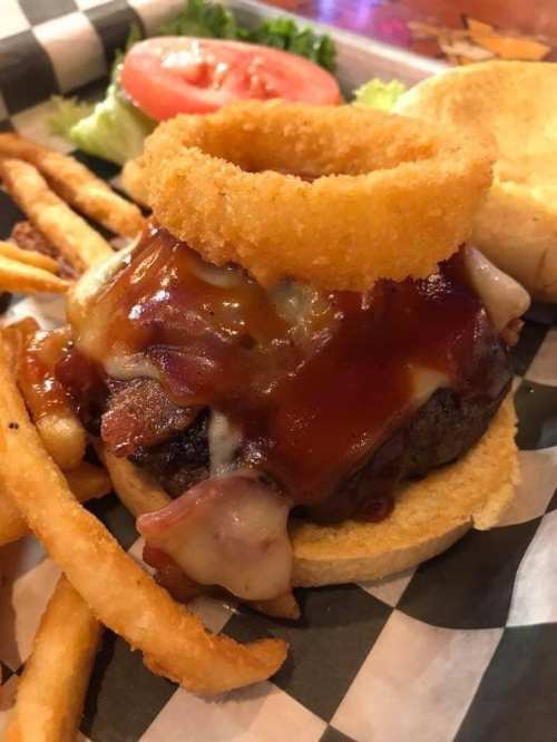 A juicy burger topped with cheese, barbecue sauce, and an onion ring, served with fries and a side of lettuce and tomato.