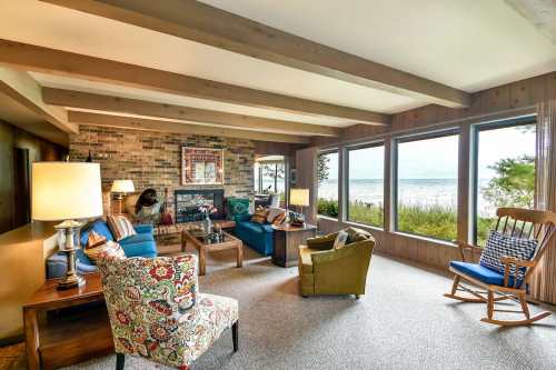Cozy living room with large windows overlooking a lake, featuring colorful furniture and a rustic design.