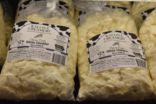Bags of Kalona Creamery white cheddar cheese curds displayed on a shelf.