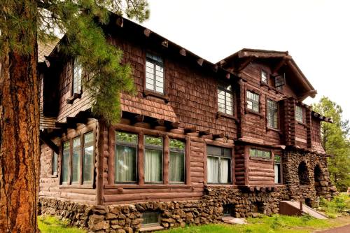 A rustic wooden lodge with large windows, surrounded by trees and featuring a stone foundation.