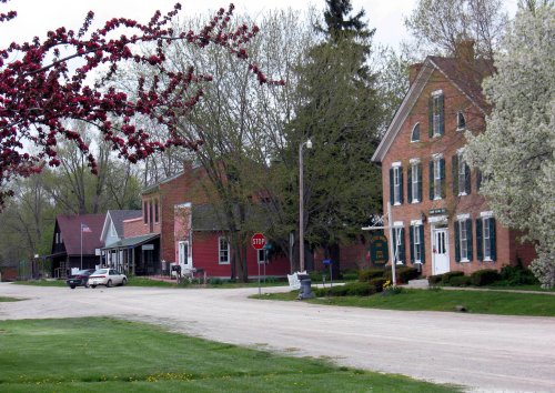 A quiet rural street lined with historic brick buildings and trees, featuring a stop sign and a parked car.