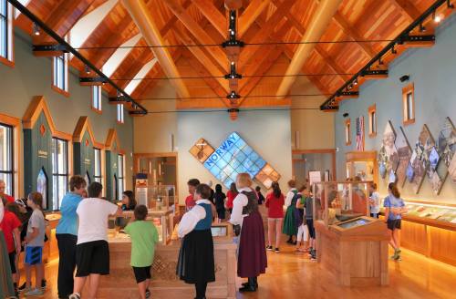 A vibrant museum interior with visitors exploring exhibits about Norway, featuring wooden architecture and displays.