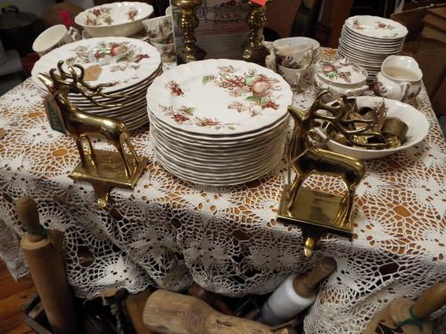 A table covered with lace, featuring decorative plates and brass deer-shaped holders among vintage dishware.