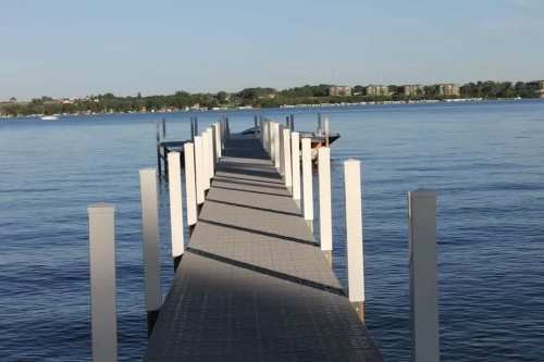A long wooden dock extends into calm water, with white posts lining the sides and a clear blue sky above.