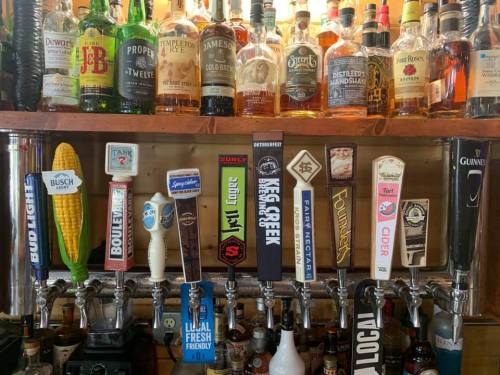 A bar display featuring various liquor bottles and beer taps, including Bud Light and Surly, with a corn decoration.