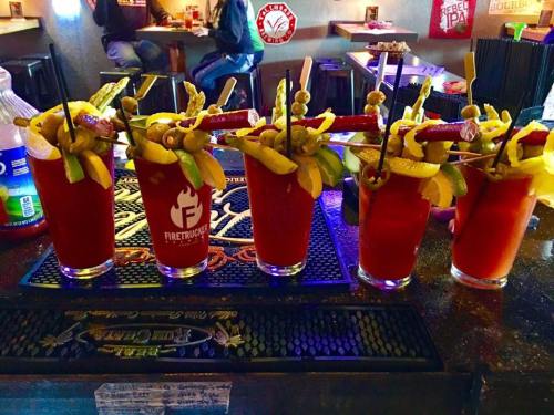 Five colorful cocktails with garnishes of olives, lemon, and lime sit on a bar counter.