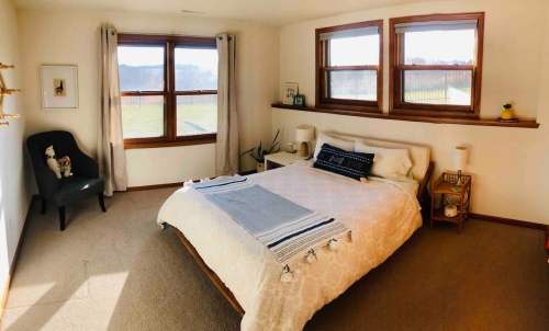 Cozy bedroom with a bed, side tables, and large windows overlooking a scenic view. Soft lighting and neutral decor.