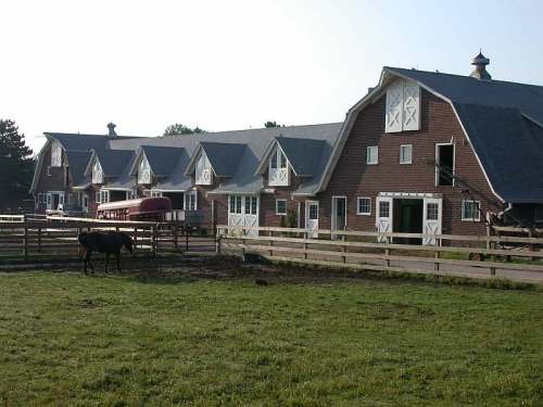 A scenic view of a red barn with white trim, surrounded by green grass and a horse grazing nearby.